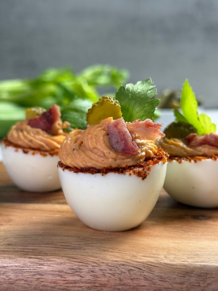 Three egg whites, filled with the yolk mix and decorated with a slice of pickle, bacon and celery leaf