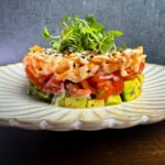 Avocado cubes layered with diced tomato and smoked salmon on a white plate