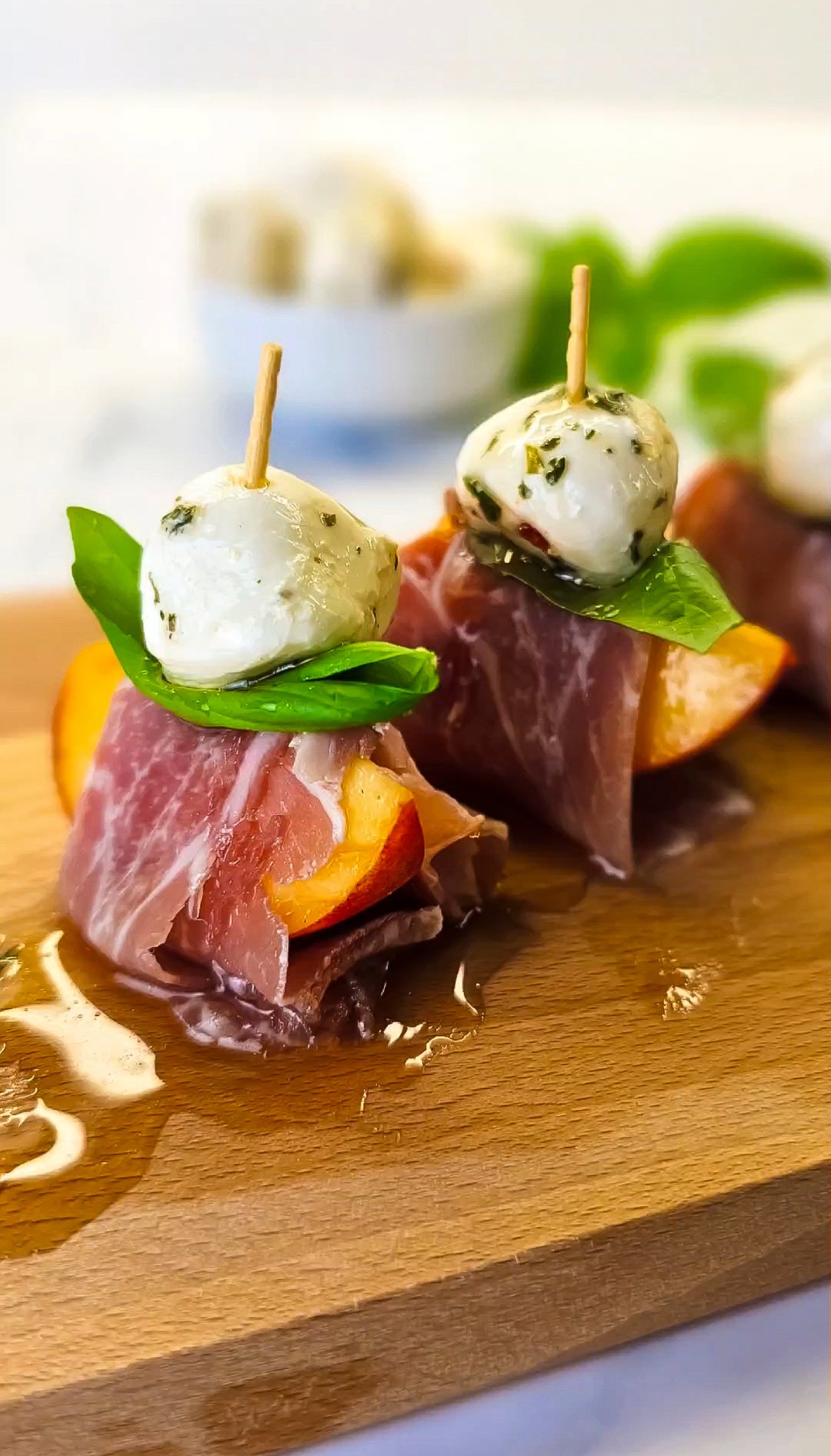 Slices of peach, wrapped with prosciutto wit basil and mozzarella balls on a wooden board.