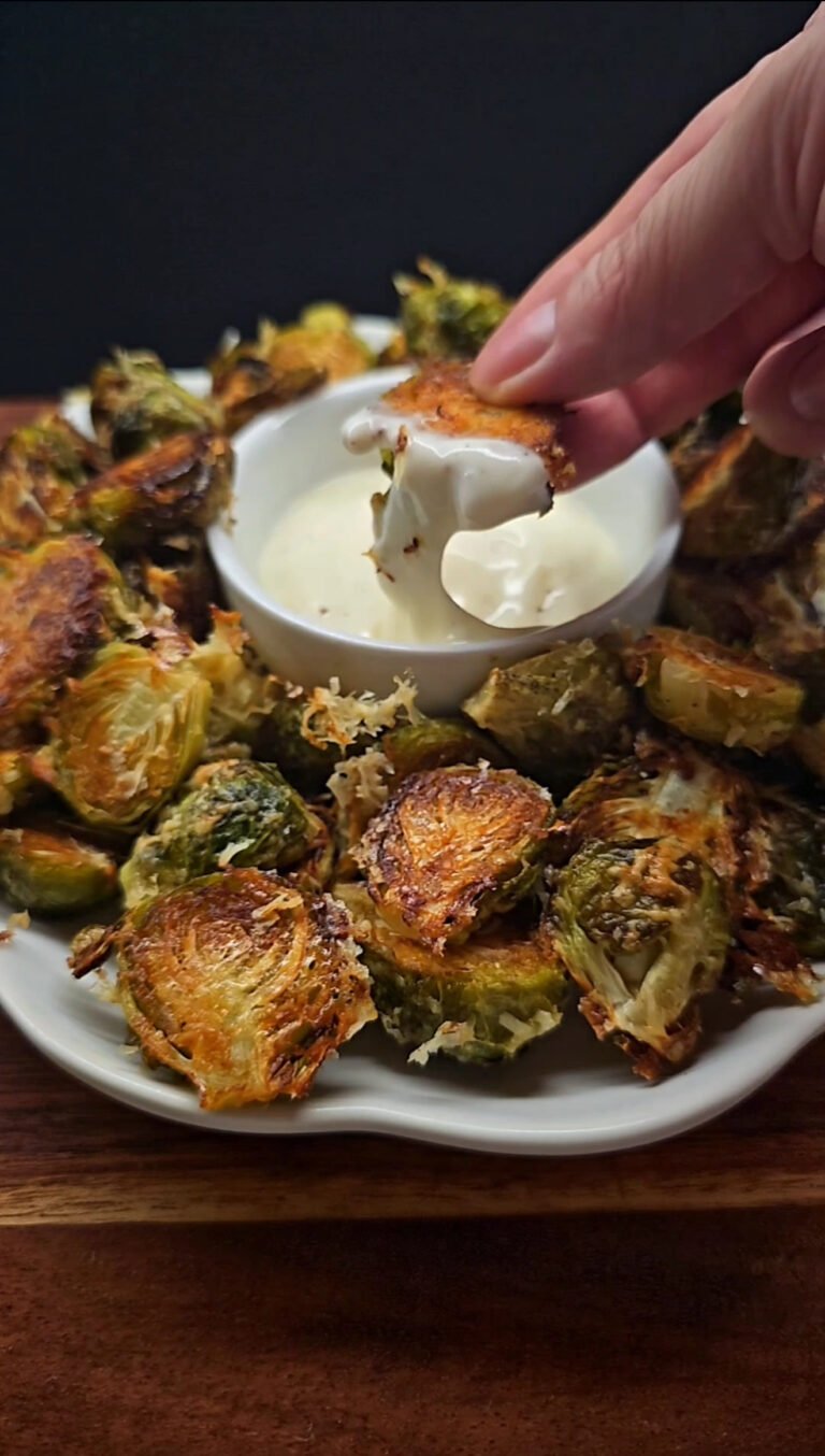 a plate with roasted Brussels sprouts. Hand is holding one of the sprouts, dipped in the sauce.
