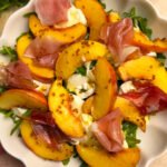 Salad with arugula, burrata, peach and prosciutto in a white bowl
