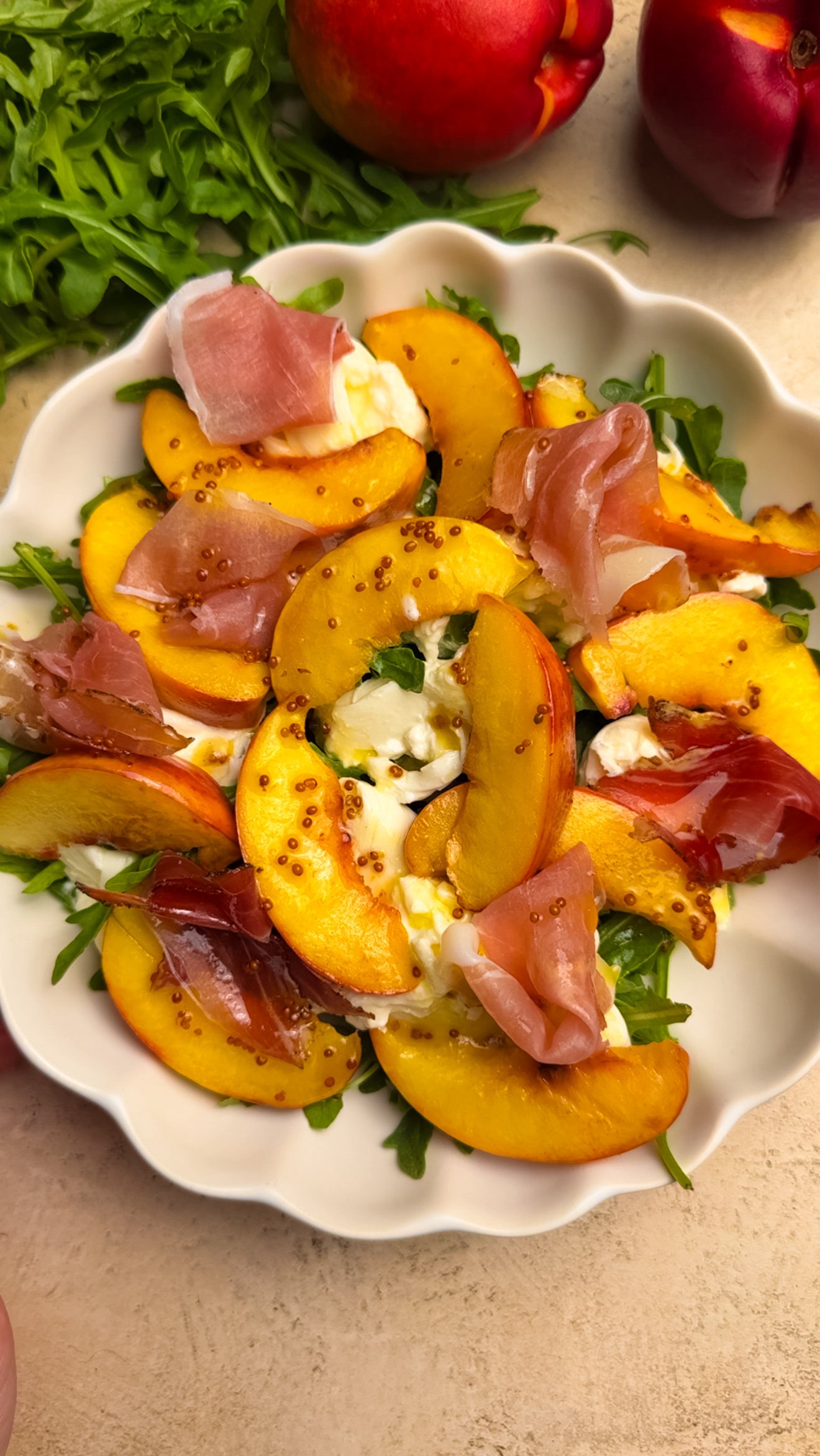 Salad with arugula, burrata, peach and prosciutto in a white bowl