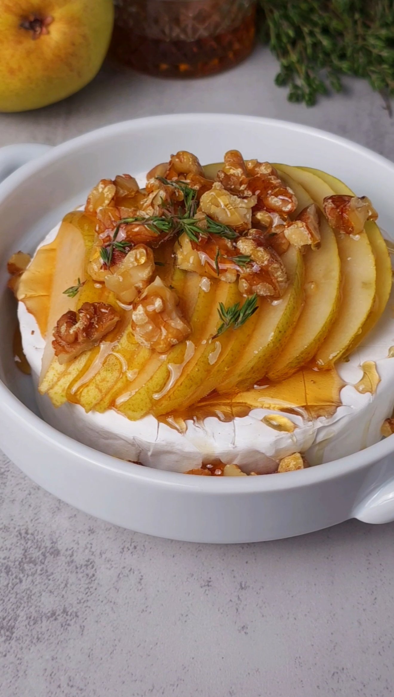 Round dish with Brie, topped with sliced pear, honey and thyme leaves