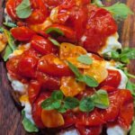 wooden board with toast, topped with cooked tomatoes