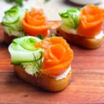 Three crostinis with salmon and cucumber on a wooden serving board
