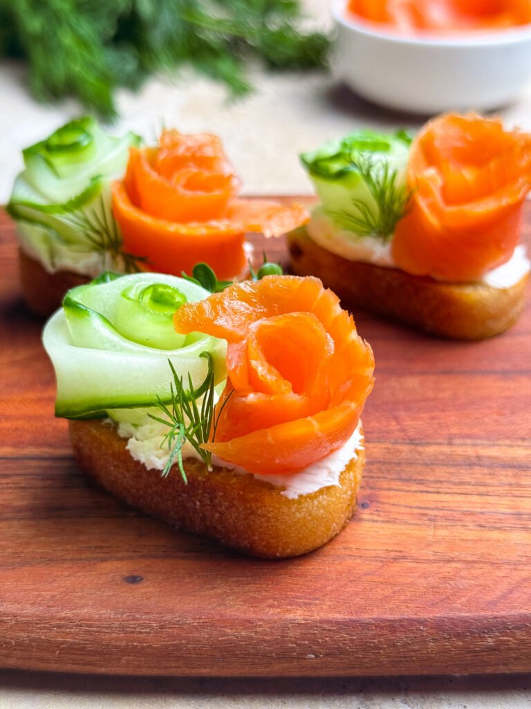 Three crostinis with salmon and cucumber on a wooden serving board