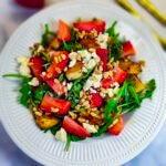 White round plate with arugula leaves, topped with fresh strawberries and fried halloumi