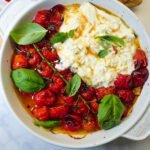 Roasted tomatoes with burrata and basil leaves in a round white baking dish
