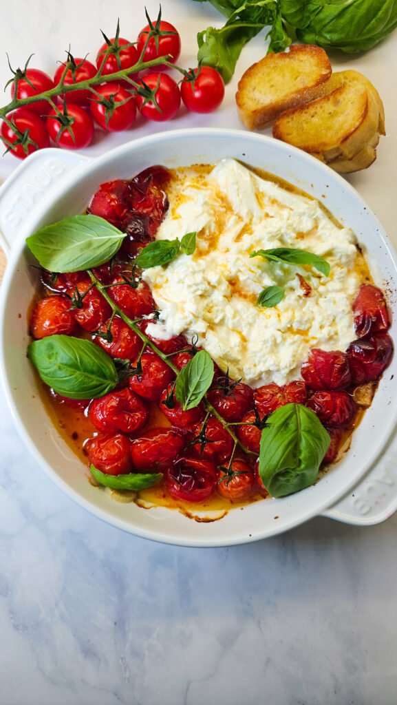Roasted tomatoes with burrata and basil leaves in a round white baking dish