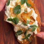 Fingers holding half a toast with cheese and herbs