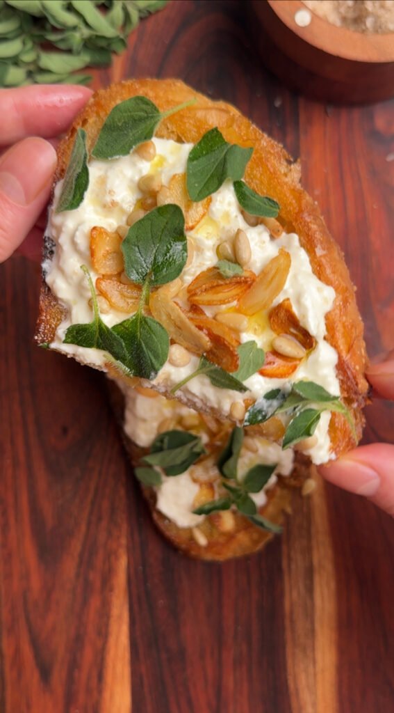 Fingers holding half a toast with cheese and herbs.