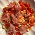 Burrata, topped with tomatoes and prosciutto in a bowl