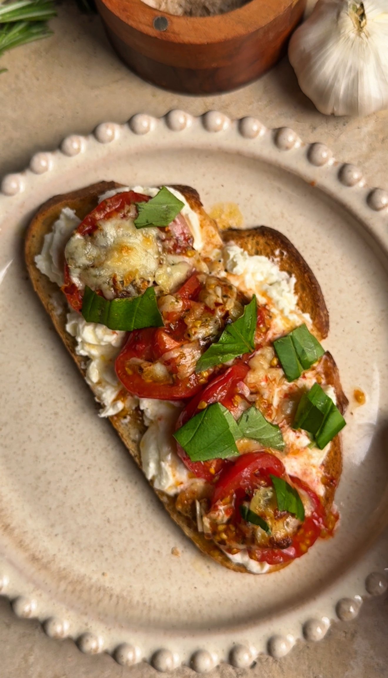 Round tan plate with a toast on it. Toast is topped with roasted tomatoes with cheese