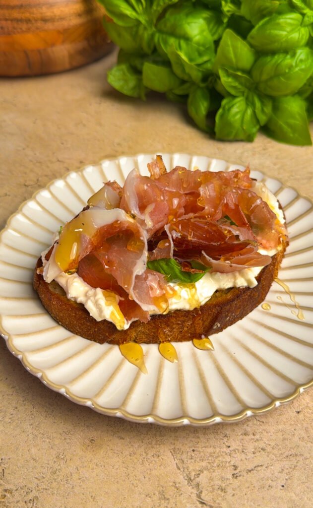 Hot Honey toast with prosciutto on a round plate. Basil in the background.