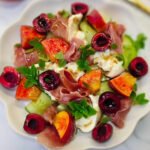Salad with peach, cherry, cucumber and prosciutto in a round plate