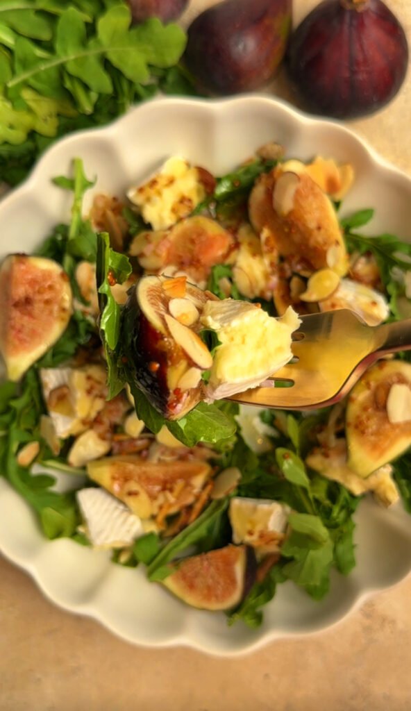 Fig salad on a plate, fork is holding cheese, fig and arugula bite