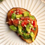Toast with tomato and avocado on a white round plate