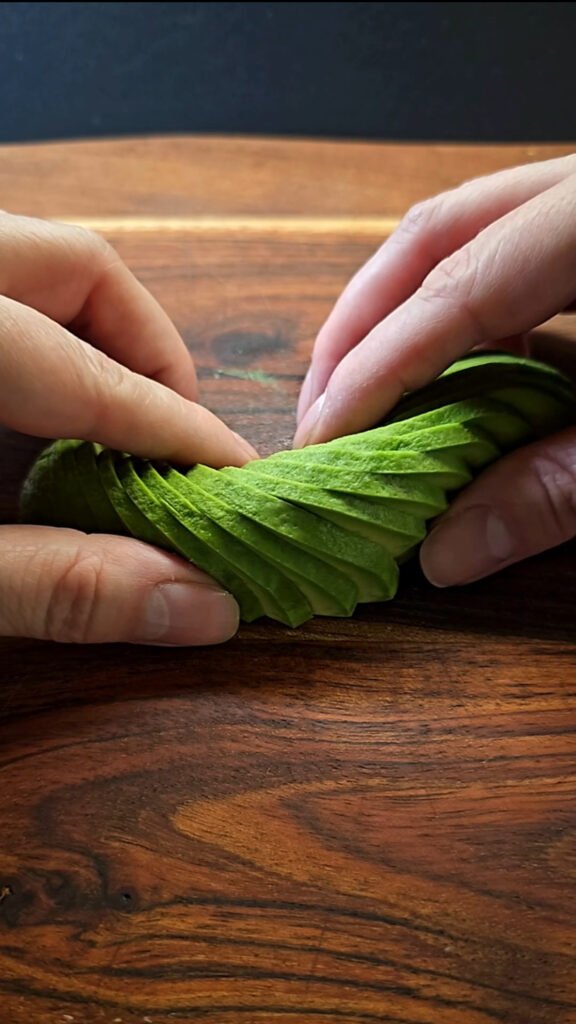 Sliced avocado on a wooden board, Hands shaping avocado.