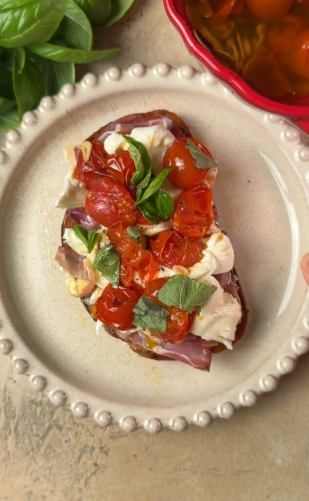Plate with a toast on it. Toast is topped with burrata and tomatoes