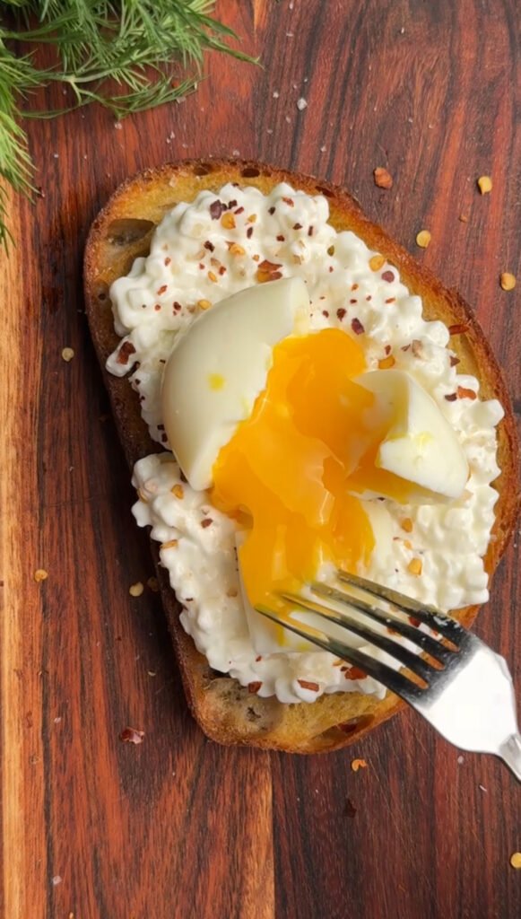 toast on a wooden board. Fork is breaking the egg with liquid yolk