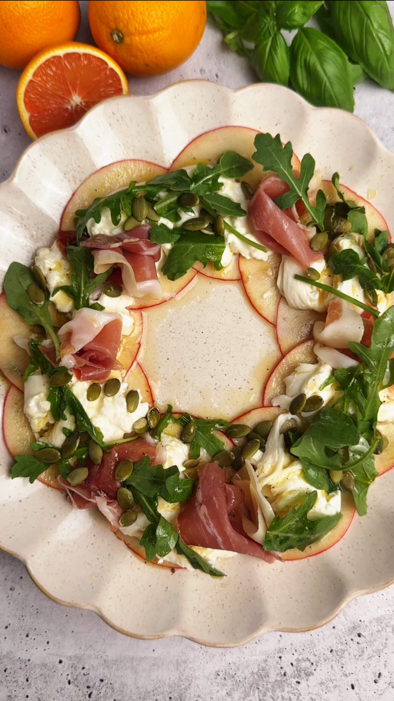 Close-up of a beautiful apple burrata and prosciutto salad wreath, topped with fresh arugula and pumpkin seeds, drizzled with orange honey dressing.