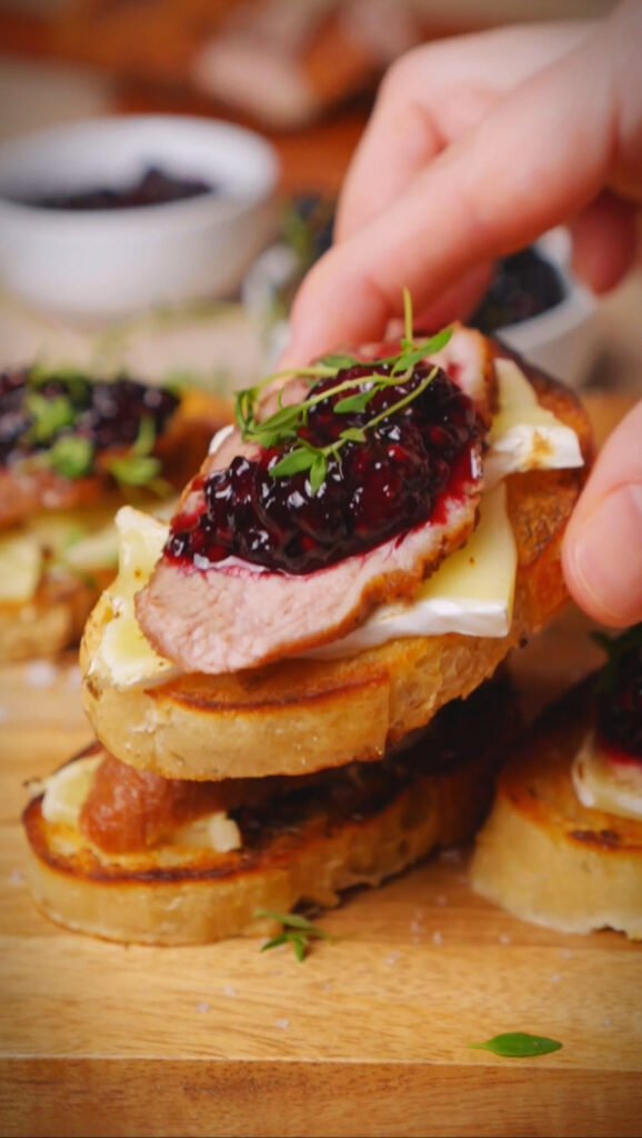 Hand is holing duck crostini with blackberry jam