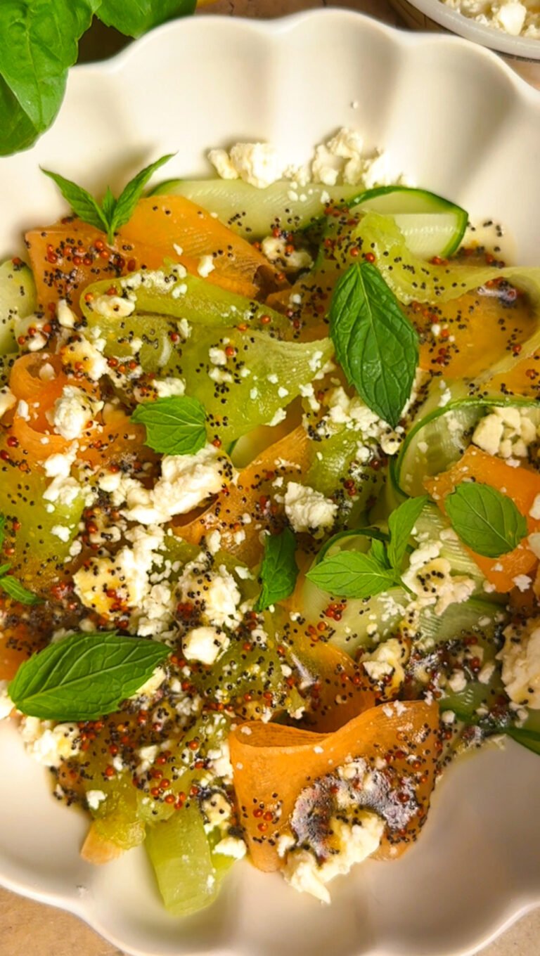Salad with melon and cucumber, topped with mint leaves on a white plate