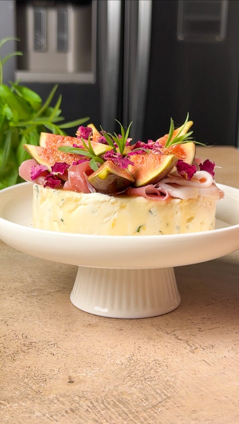 Goat Cheese & Fig Stack appetizer layered with prosciutto, figs, and hot honey on a white pedestal stand