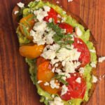 Close-up of toast with basil pesto, avocado, blistered cherry tomatoes and feta crumbs