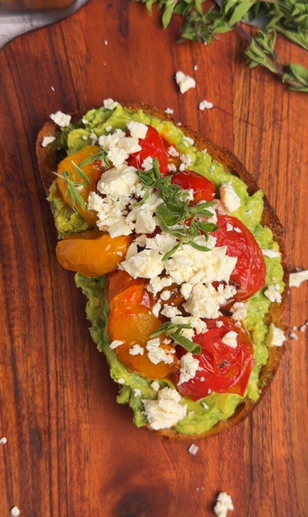 Close-up of toast with basil pesto, avocado, blistered cherry tomatoes and feta crumbs