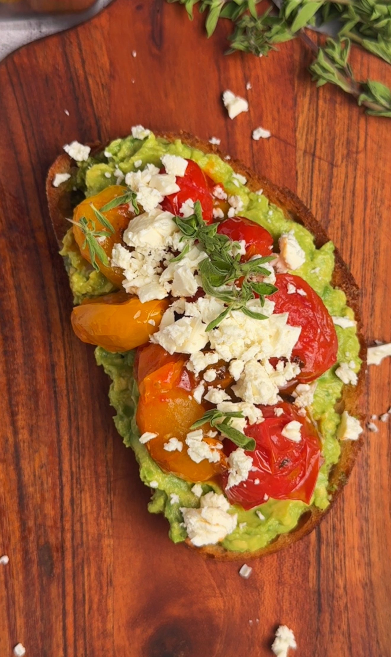 Close-up of toast with basil pesto, avocado, blistered cherry tomatoes and feta crumbs