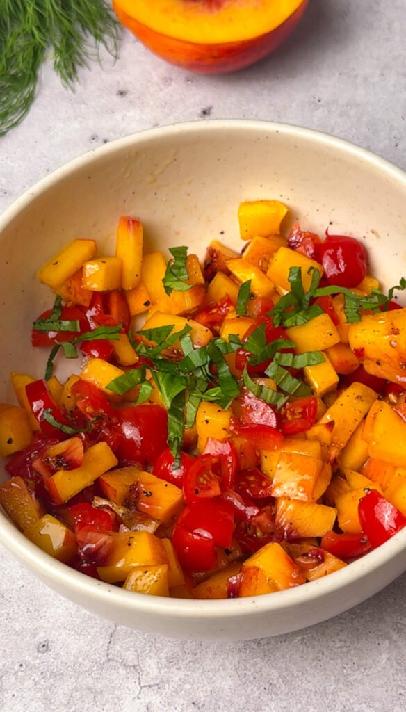 Bowl of diced peaches, cherry tomatoes, and fresh basil tossed with olive oil, salt, and pepper for peach bruschetta topping