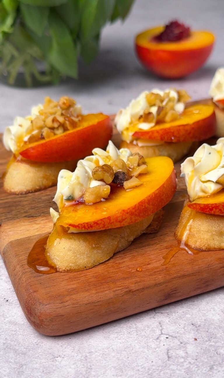 Close-up of peach and Cambozola crostini topped with chopped walnuts and honey drizzle on a wooden serving board