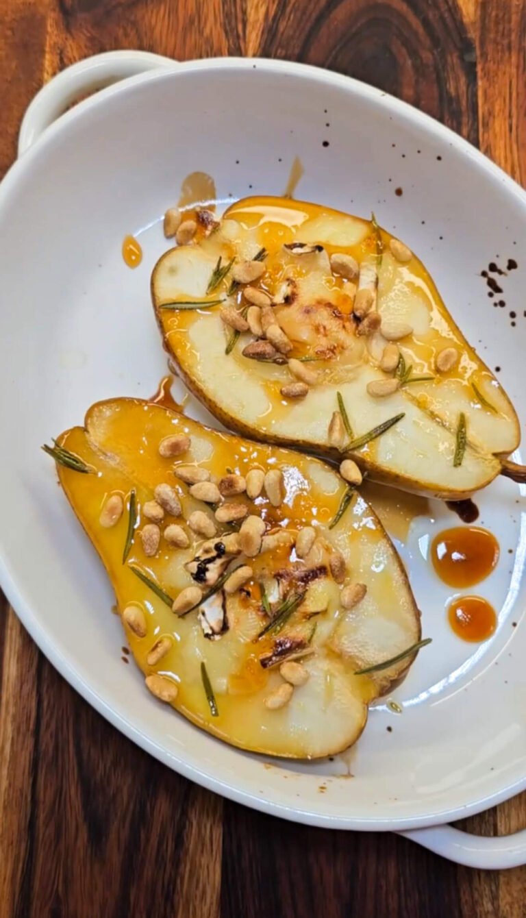 Oven-baked pear halves topped with melted Brie, toasted pine nuts, honey drizzle, and rosemary in a white serving dish