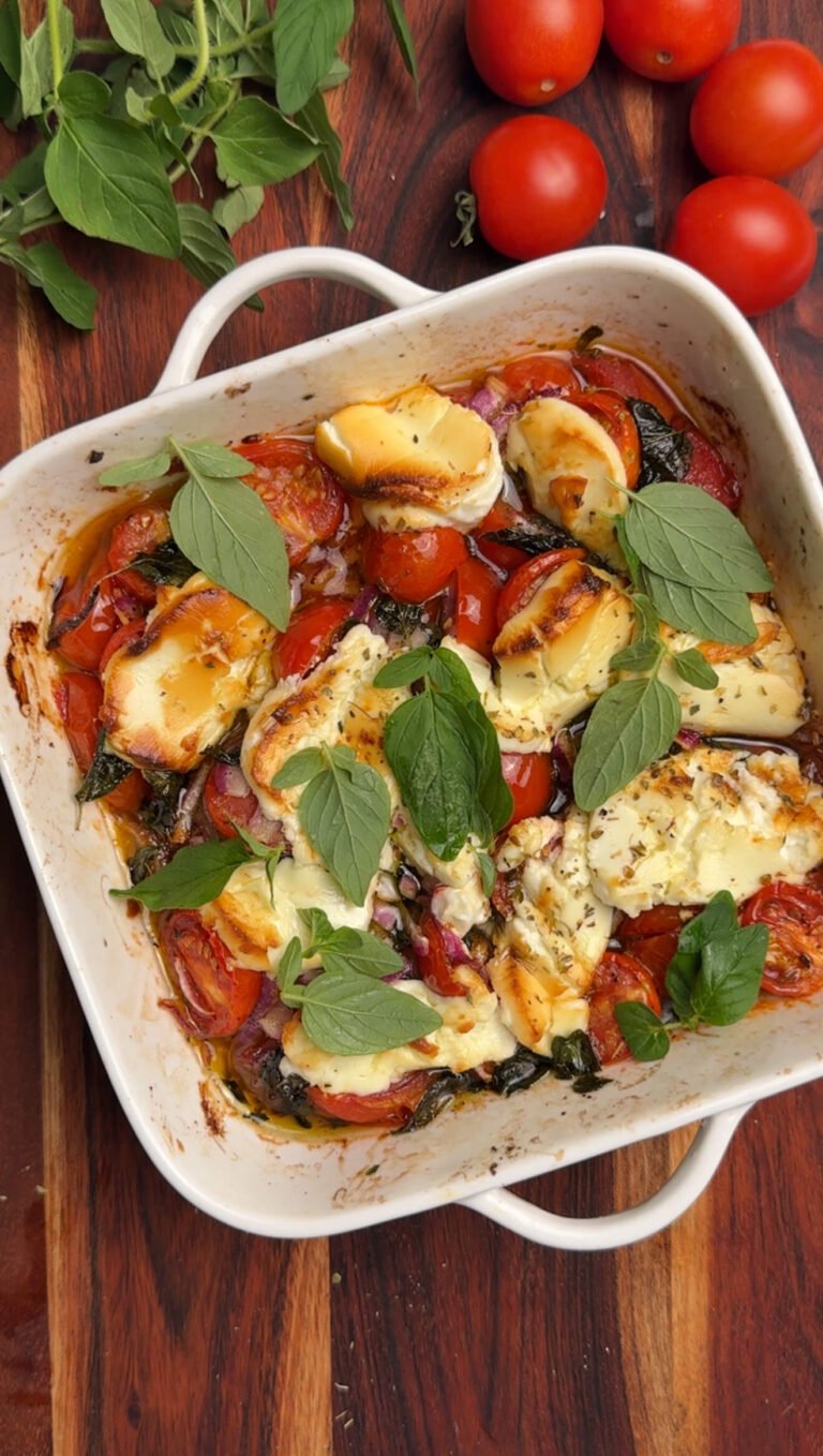 Golden, bubbly tomato bake with goat cheese in a white baking dish, garnished with fresh oregano leaves.