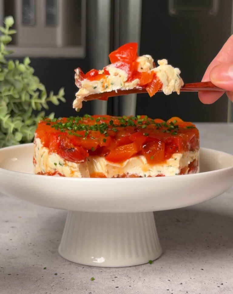 A serving of roasted pepper and cheese stack lifted from the dish, showing layers of roasted bell peppers, herbed goat cheese, and cream cheese.