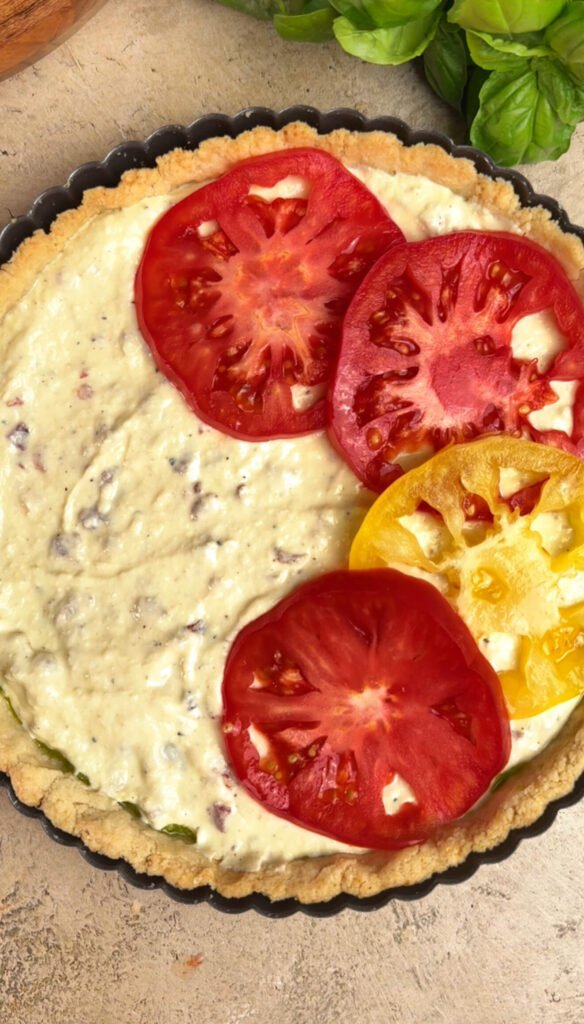 Colorful heirloom tomato slices, red and yellow, layered over ricotta and bacon filling inside tart crust