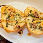 Baked Gorgonzola Pear halves topped with melted blue cheese, toasted walnuts, fresh thyme, and golden honey drizzle served in a white ceramic dish