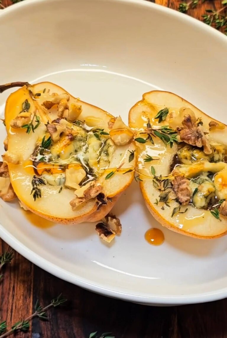 Baked Gorgonzola Pear halves topped with melted blue cheese, toasted walnuts, fresh thyme, and golden honey drizzle served in a white ceramic dish