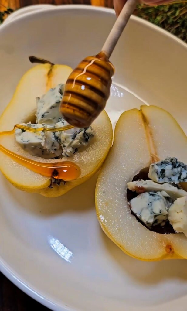 Honey drizzling over Gorgonzola-filled pear halves in a white dish, ready to bake — a sweet and savory fall appetizer