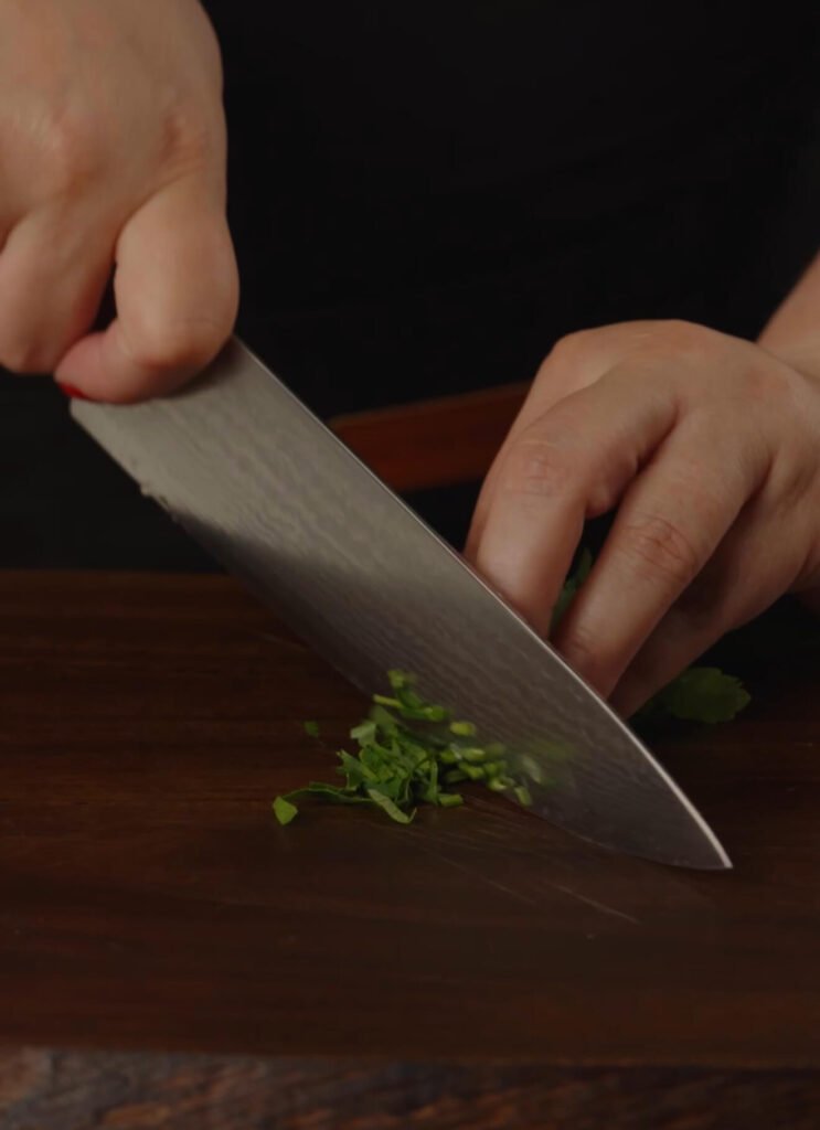 Close-up of fresh parsley being finely chopped on a dark wooden cutting board, ready to garnish the Portobello Shakshuka.