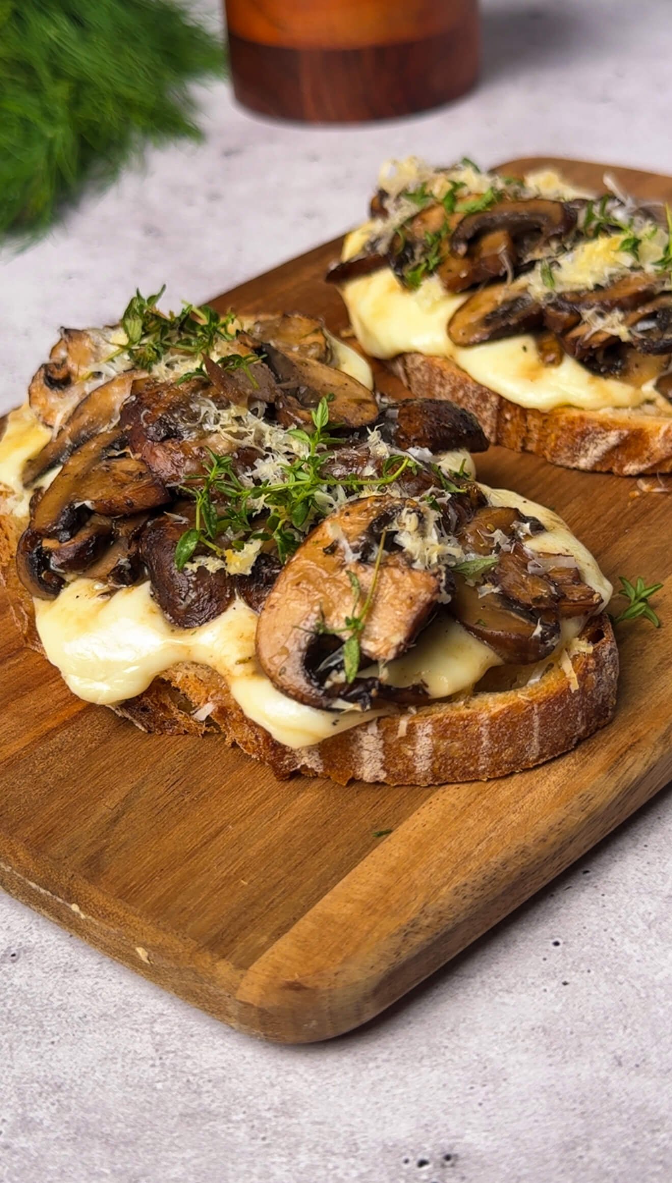 Finished double cheese mushroom toasts on a wooden board, topped with fresh thyme and melted mozzarella bubbling beneath caramelized mushrooms. The scene evokes a warm, rustic, and cozy fall feeling