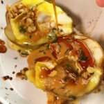 Warm baked pear topped with melted brie, creamy peanut butter, toasted walnuts, and fresh thyme as maple syrup is being poured over