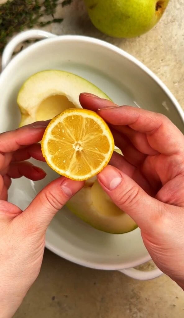Hands holding a halved lemon to drizzle juice over sliced pears before baking to add brightness and prevent browning