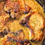 Golden-seared bone-in pork chops simmering in a rich, creamy peppercorn sauce inside a cast-iron skillet, garnished with fresh thyme. The sauce has a velvety texture with visible specks of black pepper, highlighting the cozy, rustic feel of this comforting weeknight dinner.
