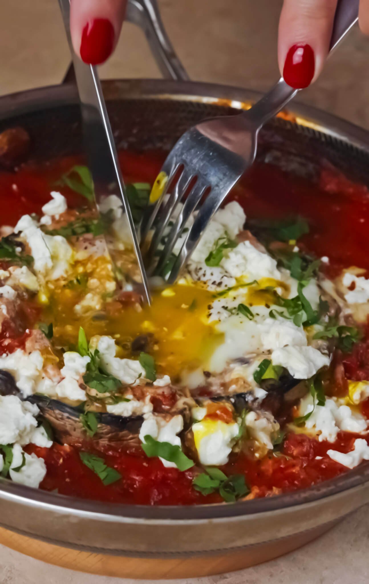Portobello Shakshuka served in a skillet — a fork cutting into the mushroom cap as the golden egg yolk flows into the tomato sauce, topped with feta and fresh herbs.