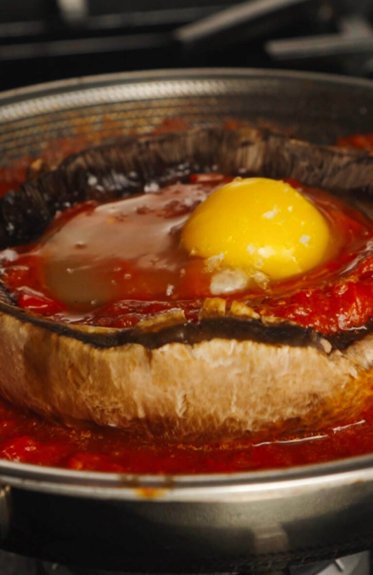 Unbaked Portobello mushroom cap filled with rich tomato sauce and a raw egg yolk in the center, ready to go into the oven for shakshuka.
