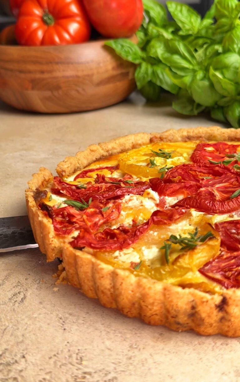 Heirloom tomato pie with red and yellow tomato slices, creamy ricotta filling, and golden flaky crust being cut, with fresh basil and tomatoes in the background