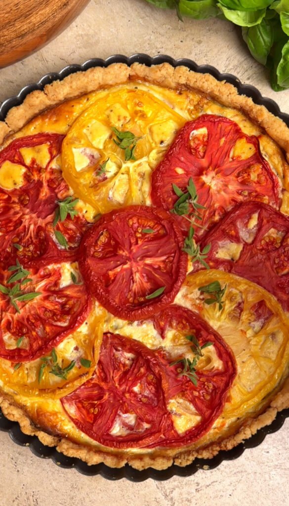 Golden baked heirloom tomato pie with ricotta, bacon, and basil pesto, topped with roasted red and yellow tomato slices and fresh herbs