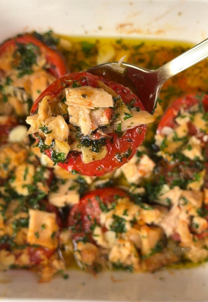 Close-up of a roasted tomato filled with tuna, parsley, and olive oil on a spoon — juicy, garlicky, and perfectly caramelized.